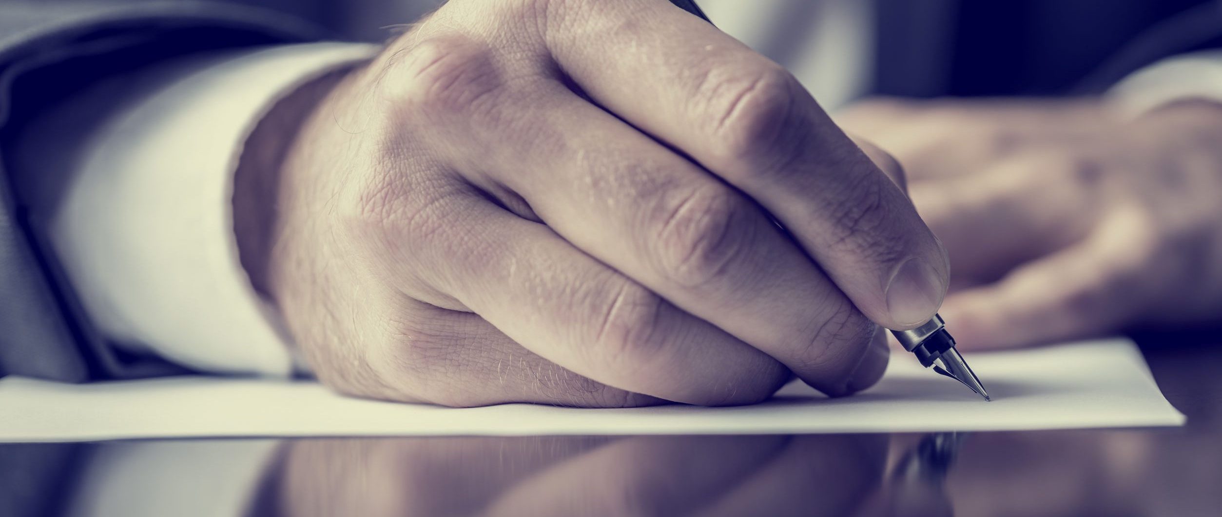 Man signing a document or writing correspondence with a close up view of his hand with the pen and sheet of notepaper on a desk top. With retro filter effect.