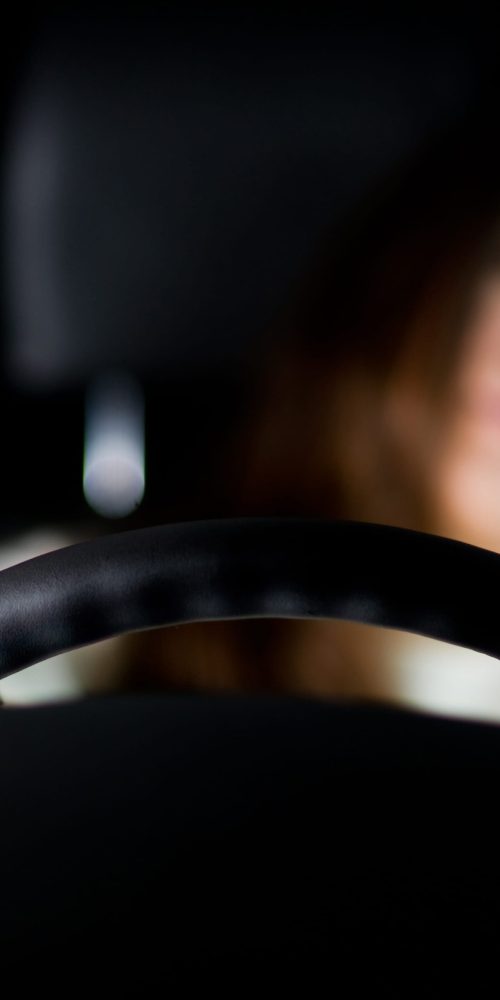 The girl leaned back in the driver's seat and holds her hands on the steering wheel, in one of her hands she has a bottle of alcohol