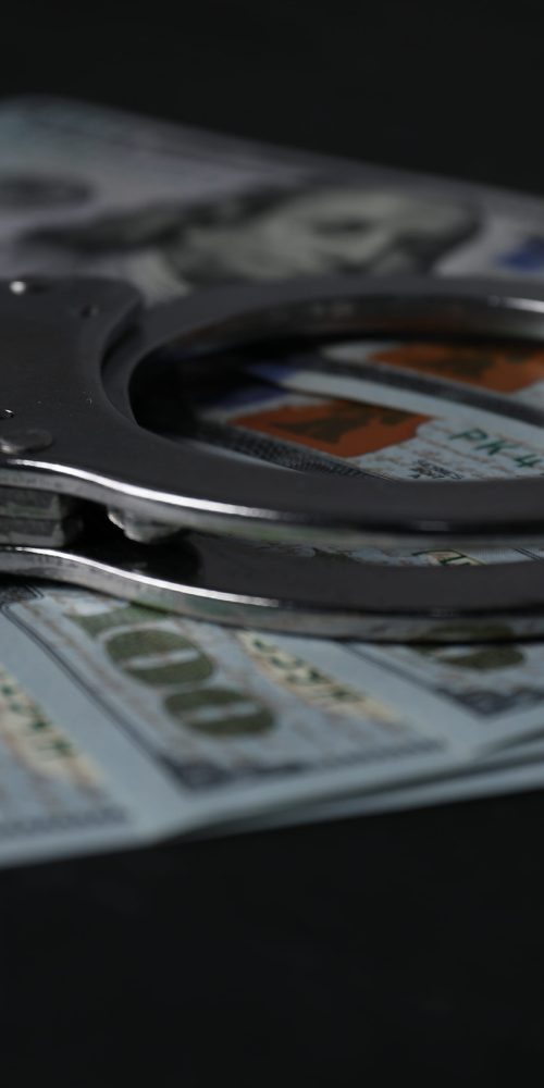 Dollar banknotes and handcuffs on black table, closeup