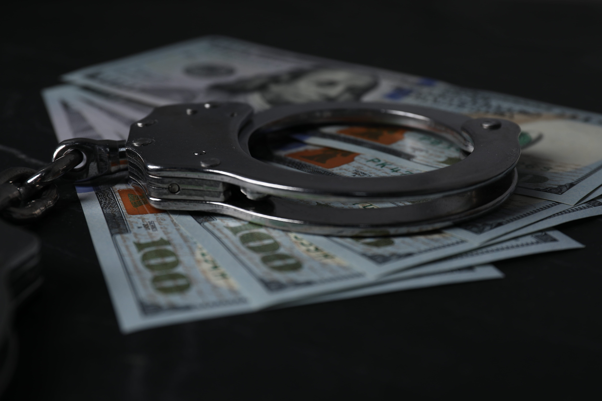 Dollar banknotes and handcuffs on black table, closeup