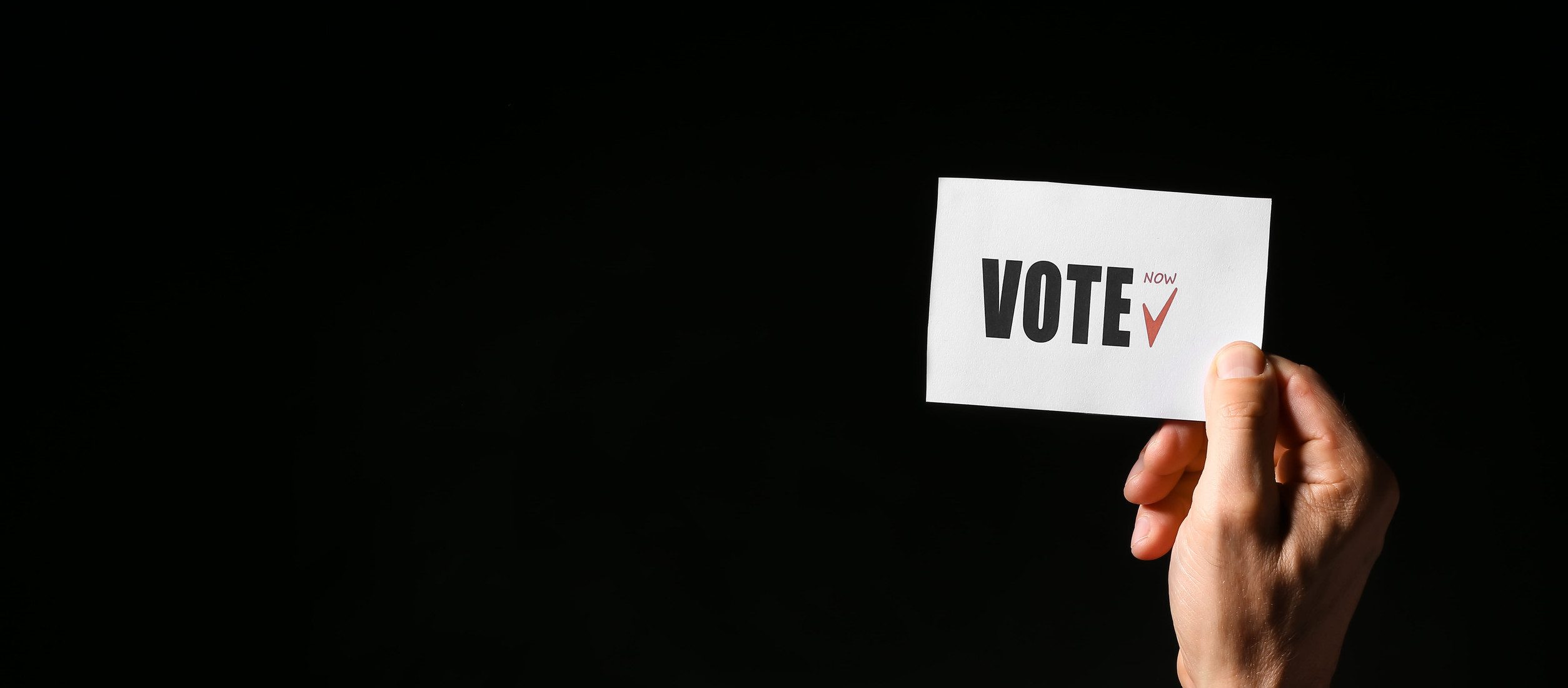 Hand holding paper with text VOTE on dark background