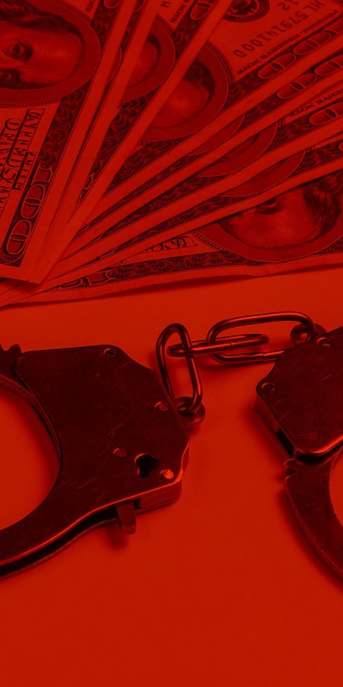 Steel handcuffs and one hundred dollar bills on in red light.