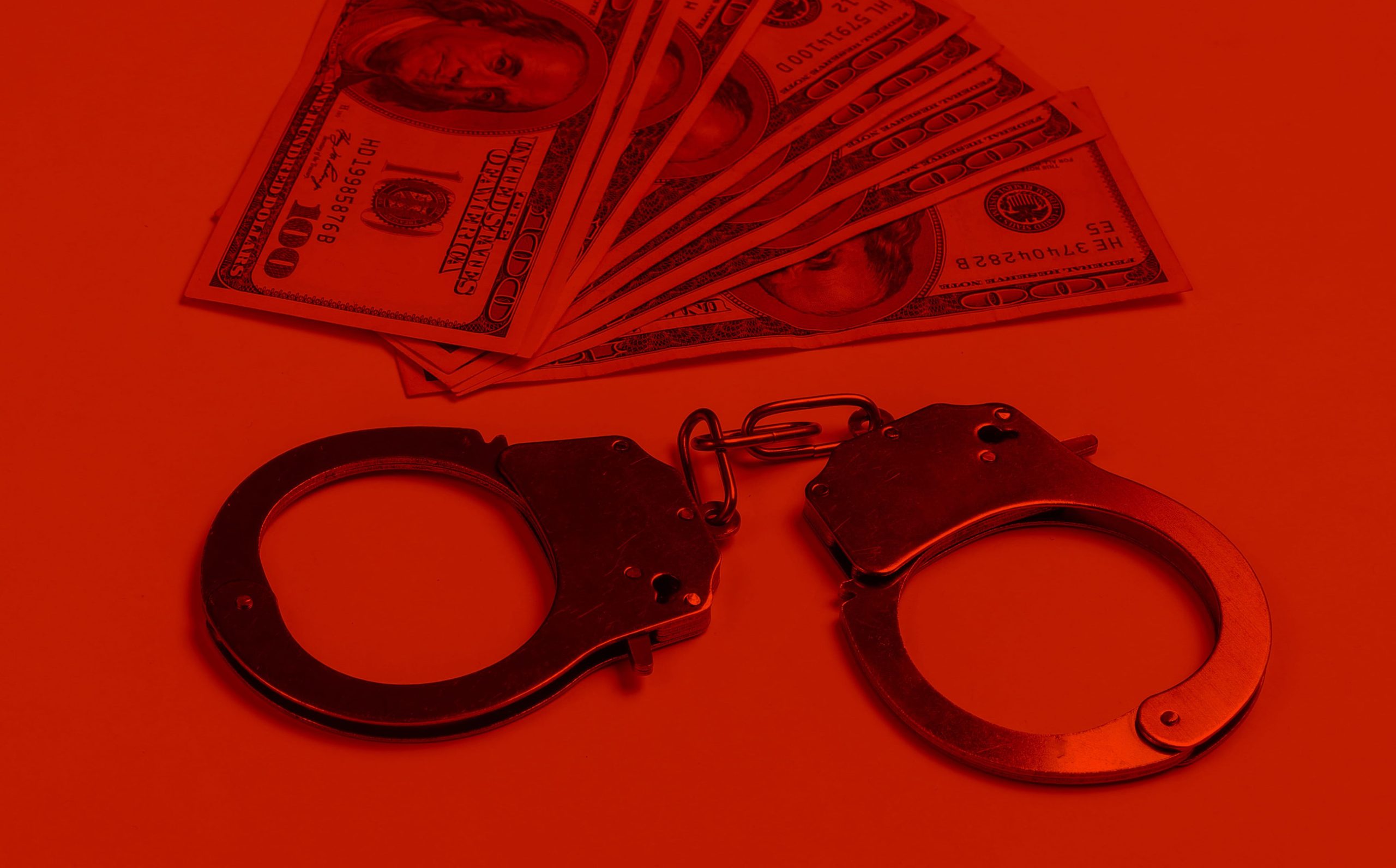 Steel handcuffs and one hundred dollar bills on in red light.