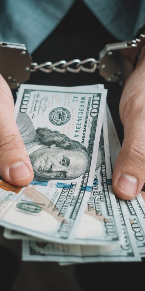 Hand with handcuffs and US dollars against dark background