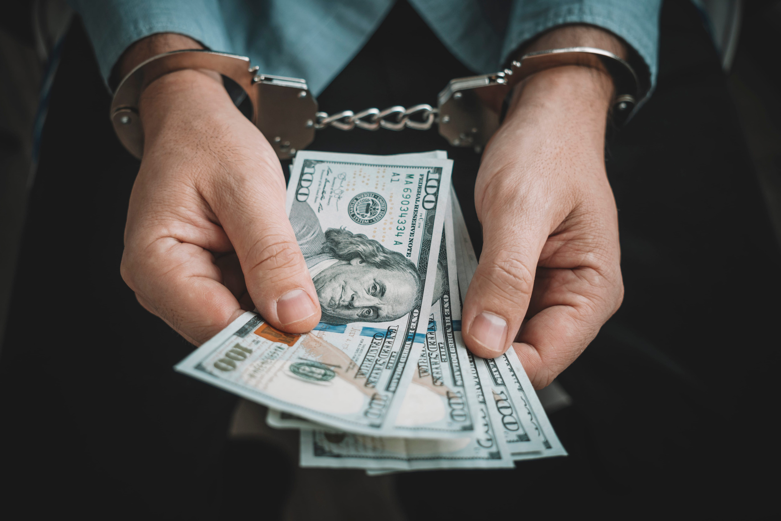 Hand with handcuffs and US dollars against dark background