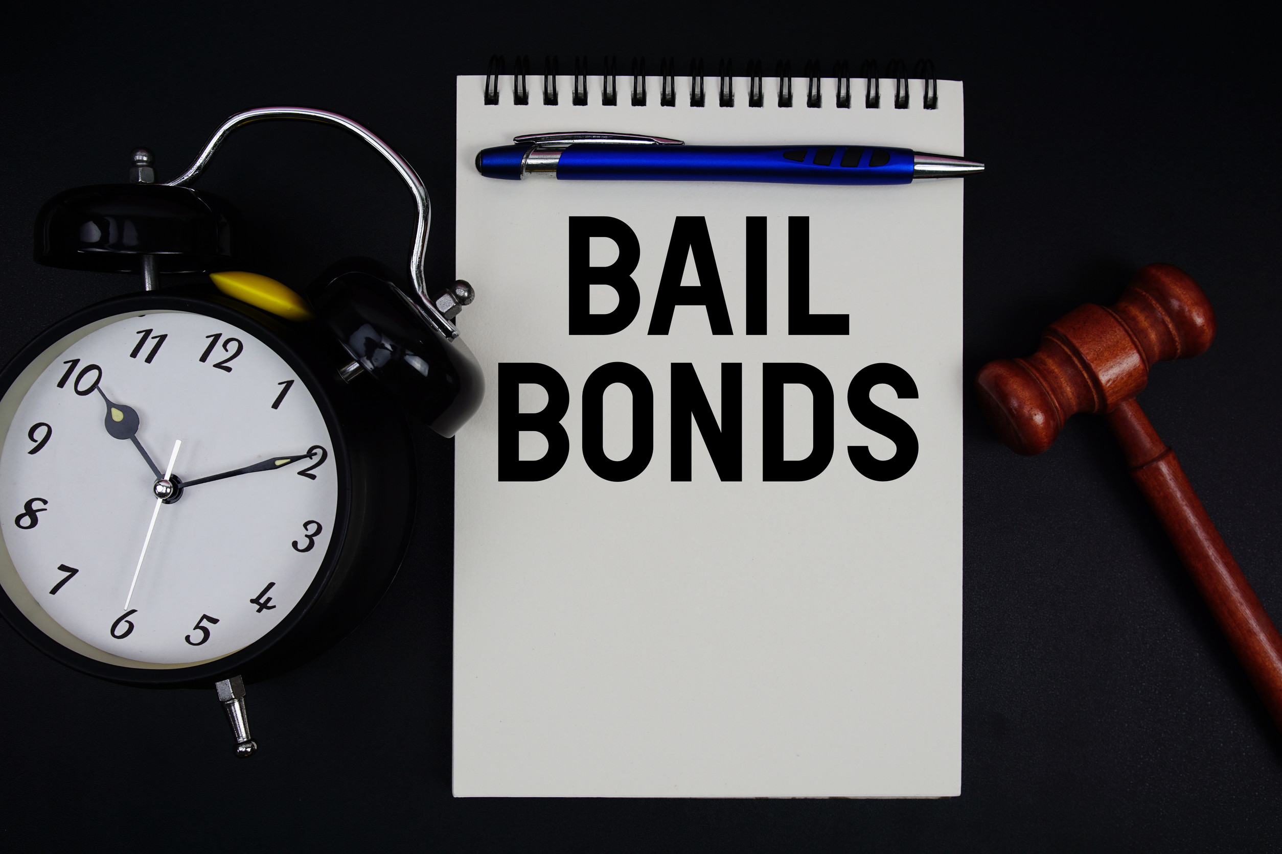 Bail Bonds text written on notepad with gavel and alarm clock on black background