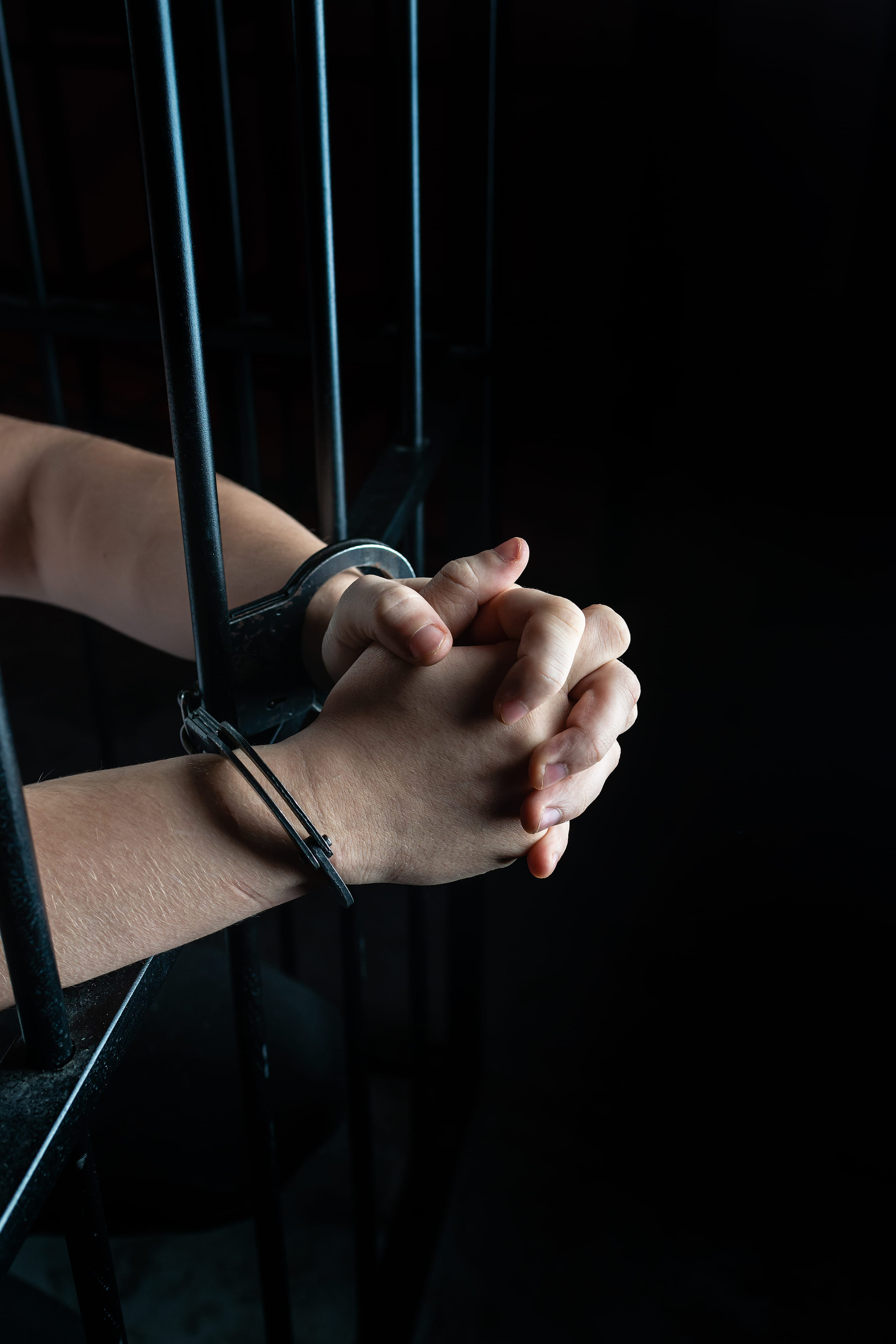 Prisoner in handcuffs praying, prisoner prays in a cell behind bars
