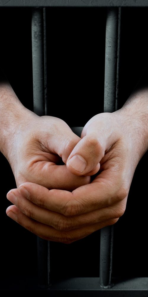 A closeup of a dimly lit prison holding cell door with arms reaching out in a folded position