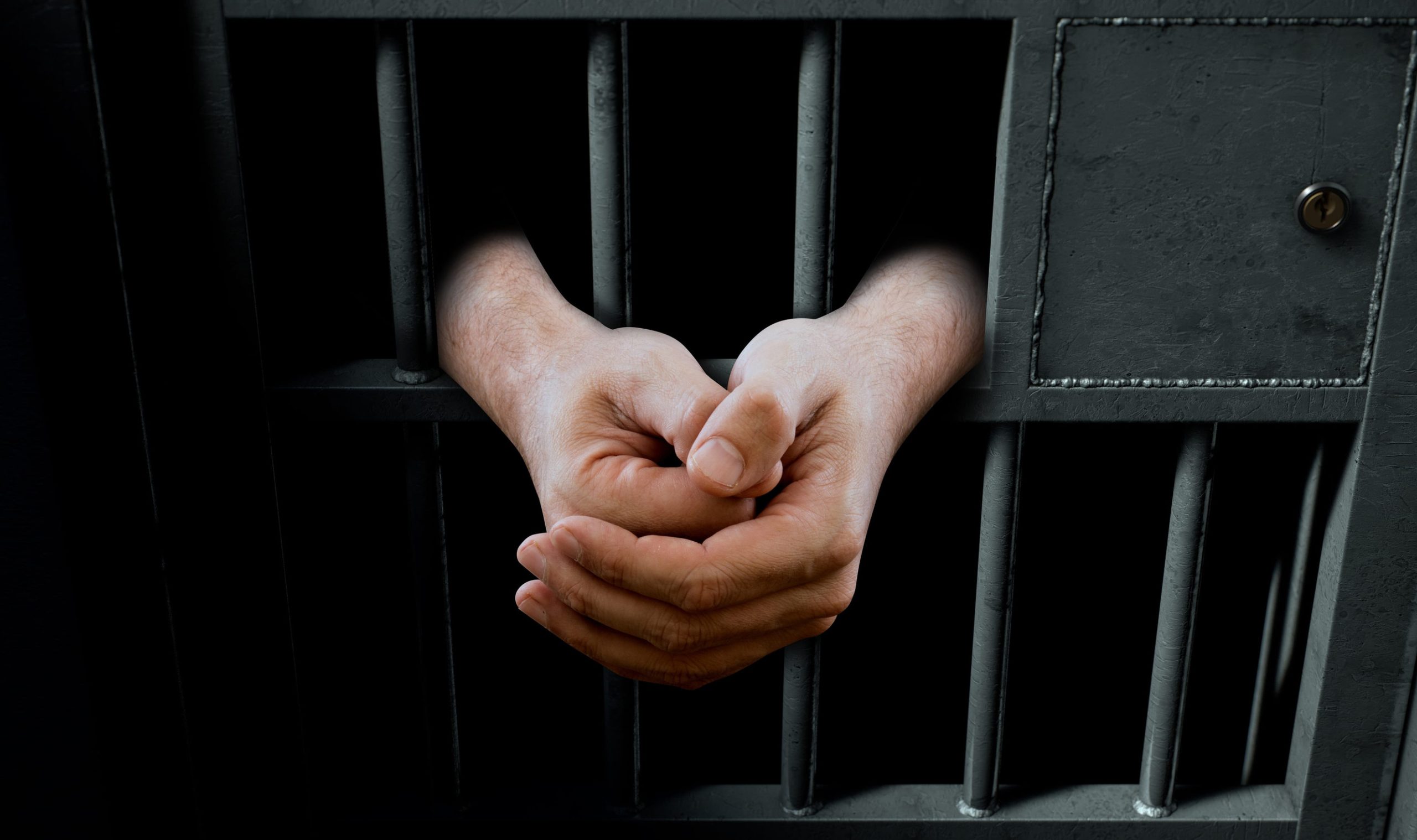 A closeup of a dimly lit prison holding cell door with arms reaching out in a folded position